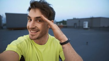 Smiling sportsman looking at camera and gesturing on roof in evening 