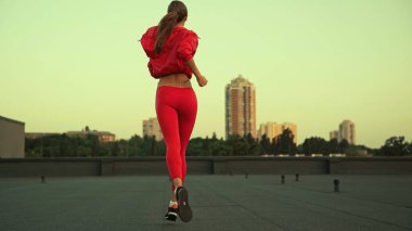 Back view of sportswoman running while training on roof in evening 