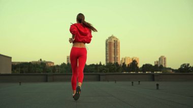 Back view of sportswoman jogging on roof in evening 
