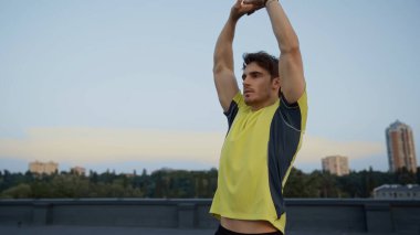 Young sportsman stretching on roof in evening 