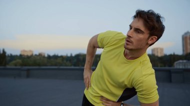 Young brunette sportsman training on blurred roof in evening 