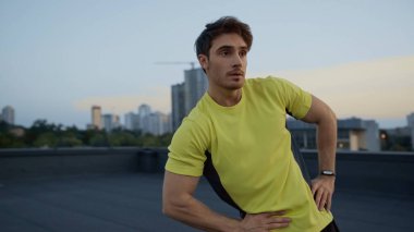 Young sportsman in yellow sportswear training on roof of building in evening 