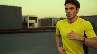 Young brunette sportsman running on roof of building in evening 