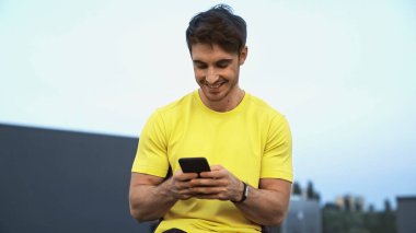 Happy young sportsman using cellphone on roof in evening 