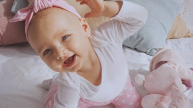 adorable baby girl with headband smiling and gesturing in baby crib at home 