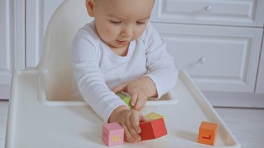 focused baby girl sitting in feeding chair and playing with wooden cubes