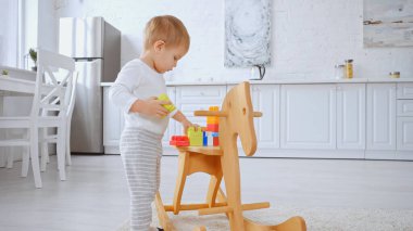 toddler child playing with building blocks on rocking horse in spacious apartment 