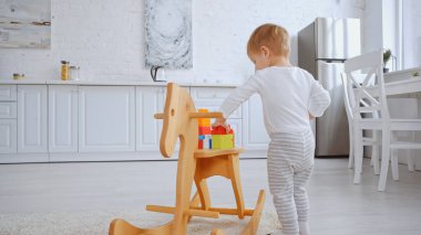 toddler kid playing with building blocks on rocking horse in spacious apartment