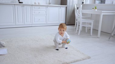 toddler boy sitting on carpet and holding small globe in spacious room