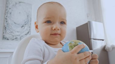 baby girl with blue eyes sitting on chair and holding small globe