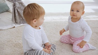 toddler brother looking at sister while sitting together on carpet at home