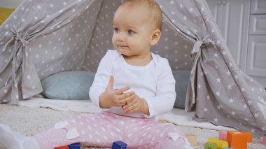 cute toddler kid sitting near multicolored wooden blocks on carpet 