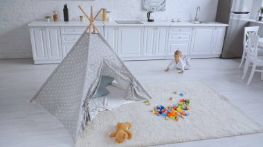 toddler boy crawling in spacious white apartment with toys and baby wigwam