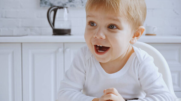 excited toddler boy with opened mouth sitting in feeding chair at home