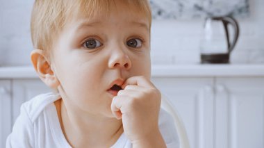 close up of surprised toddler boy touching lips and looking at camera