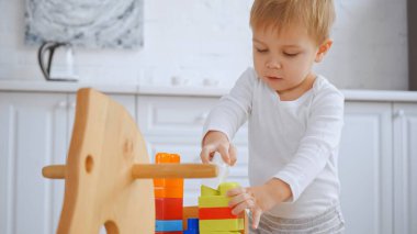 toddler boy playing with building blocks on wooden rocking horse in apartment 