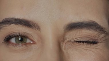 close up view of woman with hazel eyes and mascara on eyelashes winking while looking at camera 