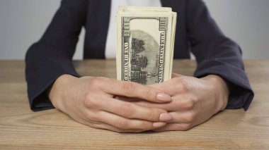 cropped view of woman in formal wear holding dollar banknotes at wooden table isolated on grey