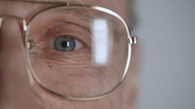 cropped view of mature man with blue eye and eyeglasses looking at camera isolated on grey  clipart