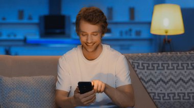 happy young man smiling while chatting on smartphone in evening 