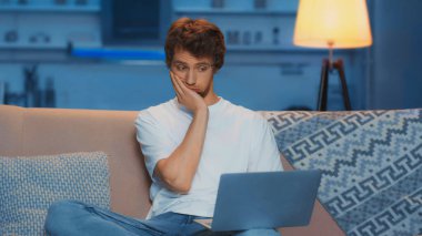 tired young freelancer touching face while using laptop and working from home in evening 