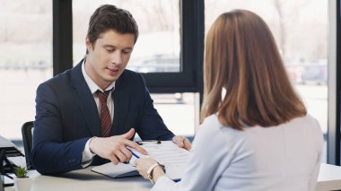 man pointing at resume during job interview with businesswoman in office clipart