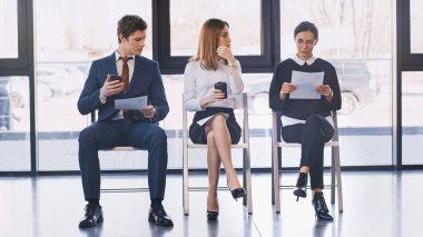 job seekers with resumes sitting near woman with takeaway drink in office