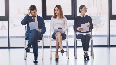 thoughtful man touching head while reading resume near job seekers waiting in office