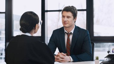 smiling businessman sitting with clenched hands while listening to woman on job interview