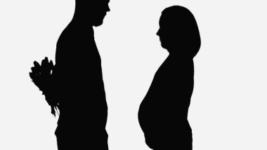 silhouette of man holding bouquet behind back near pregnant wife isolated on white