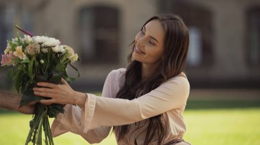 Man giving bouquet to smiling brunette girlfriend in park 