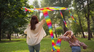 Back view of mother and child playing with flying kite in park 