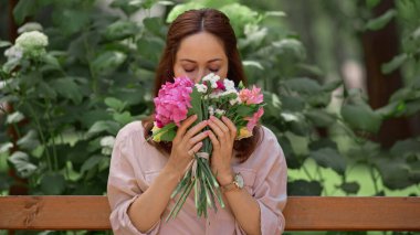 Woman smelling flowers while sitting on bench in park 