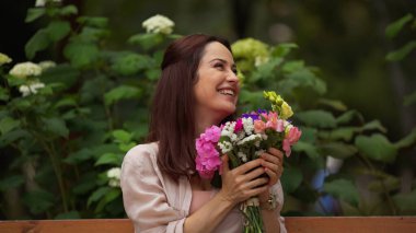 Positive woman holding bouquet in summer park 
