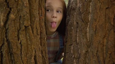 Preteen child sticking out tongue near trees in park 