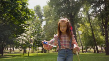 Red haired girl holding soap bubbles in summer park 