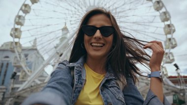 Low angle view of cheerful woman in sunglasses standing on urban street 