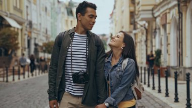 Cheerful interracial travelers looking at each other on urban street 