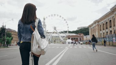 Back view of woman with backpack walking on urban street 