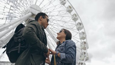 Low angle view of multiethnic tourists holding hands near blurred ferris wheel 