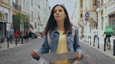 Young tourist with backpack holding map on urban street 