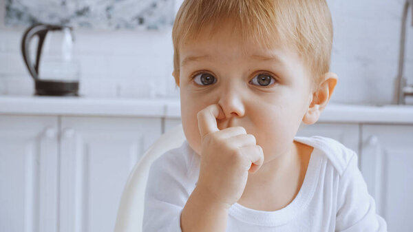 close up of toddler boy picking his nose and looking at camera at home