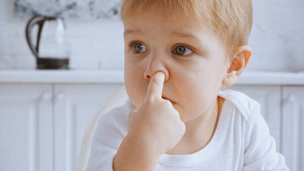 close up of naughty toddler boy picking his nose and looking away
