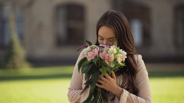 Young brunette woman smelling bouquet of flowers in park 
