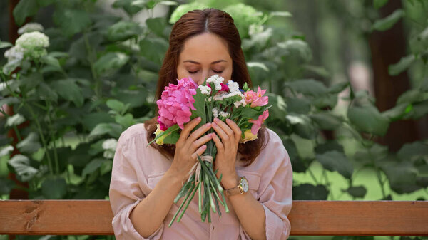 Woman smelling flowers while sitting on bench in park 