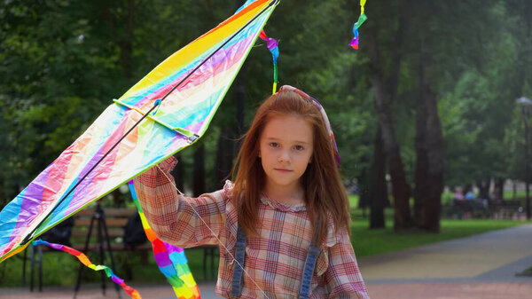 Red haired girl holding flying kite in park