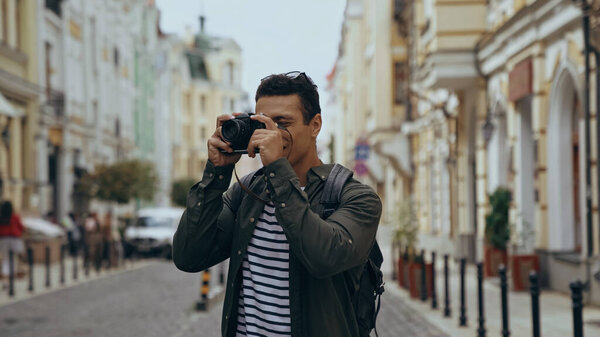 Bi-racial tourist taking photo on film camera on urban european street 