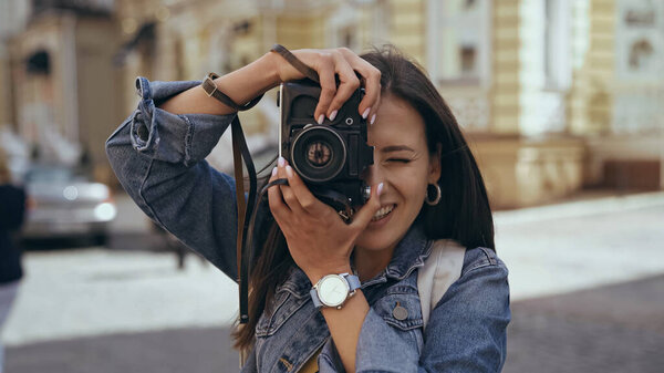 Smiling traveler taking photo on film camera on urban street 