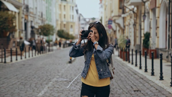 Young traveler taking photo on retro camera on urban street 