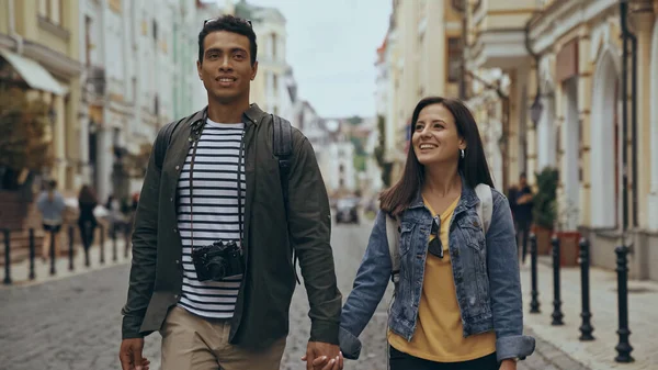 Smiling multiethnic tourists holding hands on urban street